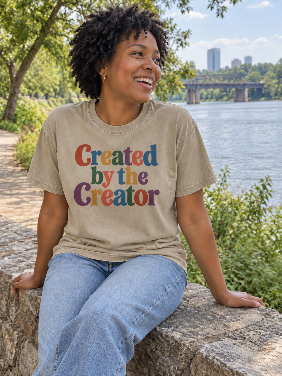 Created by the Creator Khaki tee beside a riverside trail.