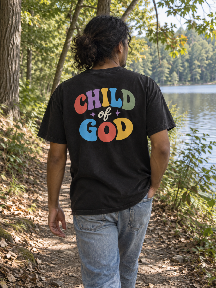 Man showing the colorful Child of God back print on a wooded lakeside trail.