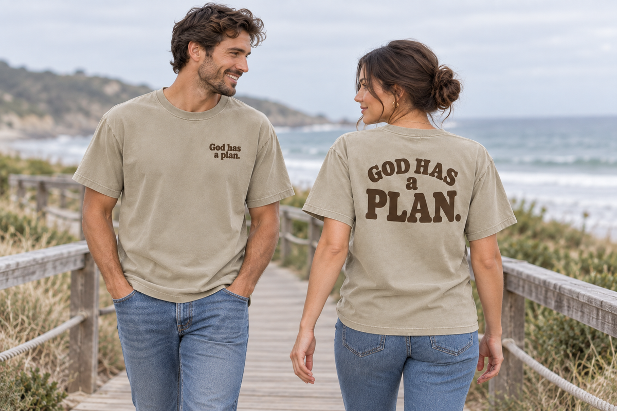 Friends wearing front and back of khaki God Has a Plan tees on a seaside boardwalk