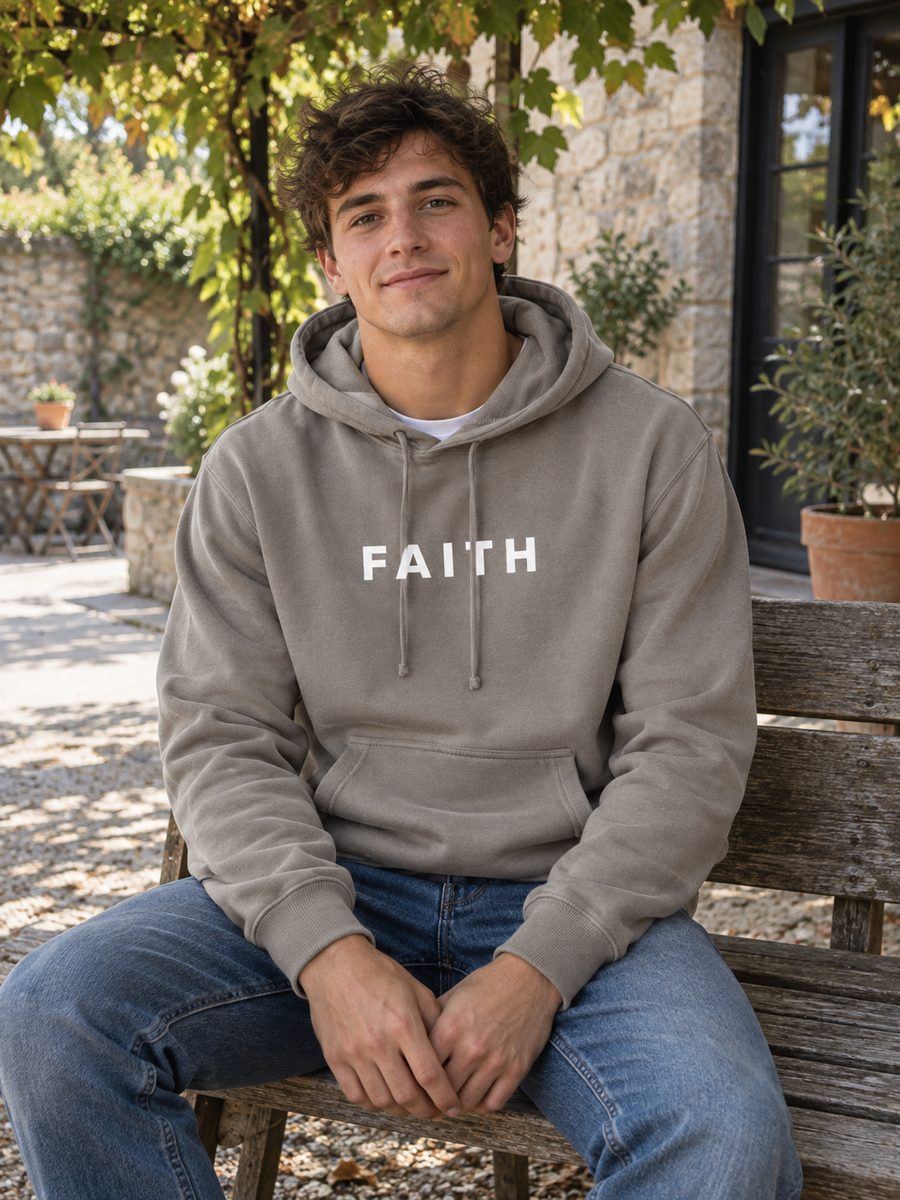 Faith Unisex Pigment-Dyed Hoodie Sweatshirt — Man seated in vine-covered courtyard