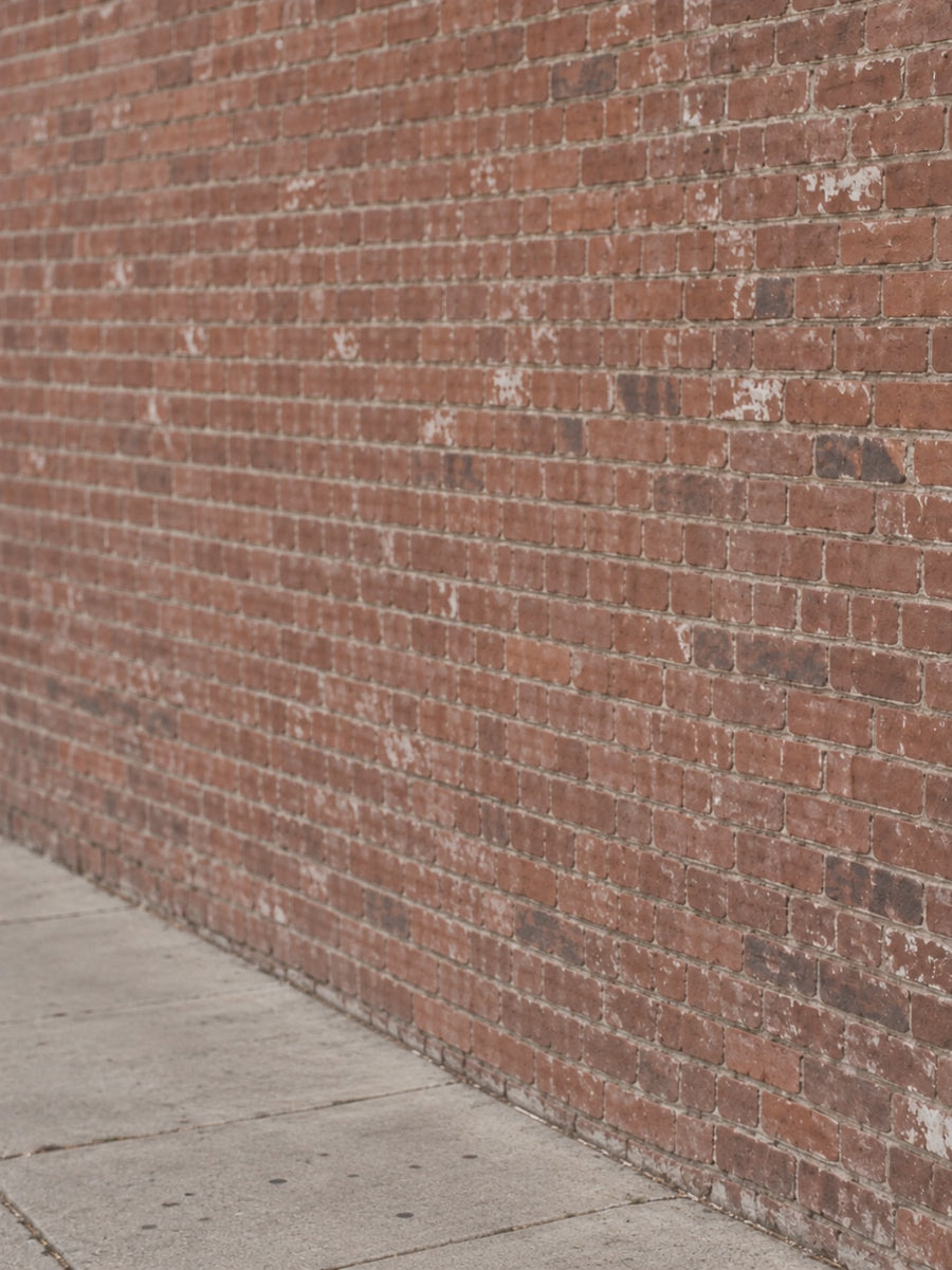 Jesus Is King black tee — candid man walking into frame beside a neighborhood brick wall