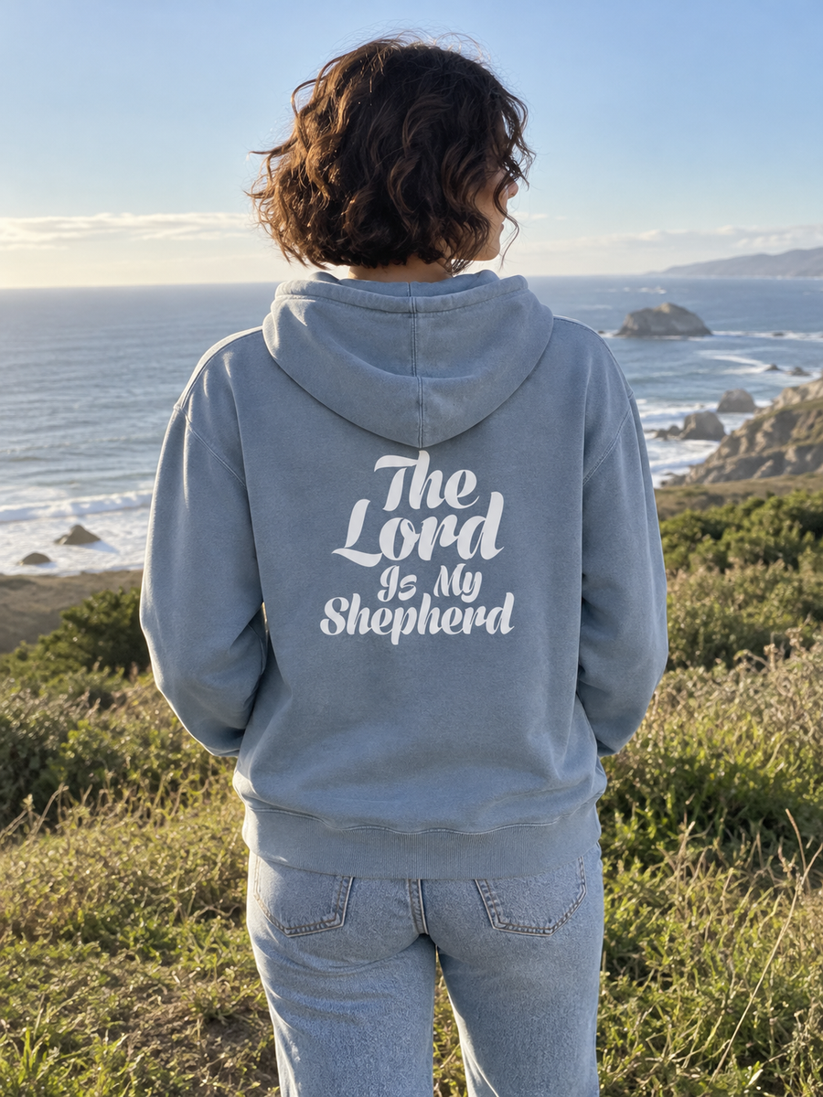 Psalm 23:1 Unisex Pigment-Dyed Hoodie Sweatshirt — Woman on coastal overlook, back print visible