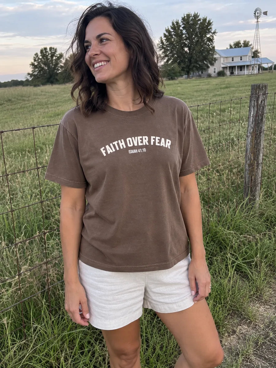 AI-created scene of a woman wearing the brown Faith Over Fear tee by a grassy field