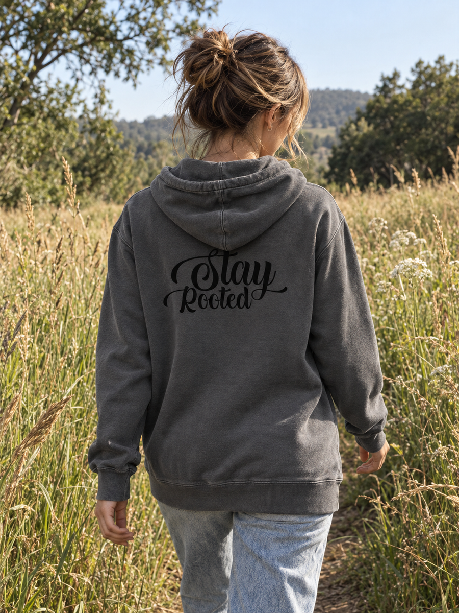 Stay Rooted Unisex Pigment-Dyed Hoodie Sweatshirt — Woman walking through meadow, back print visible