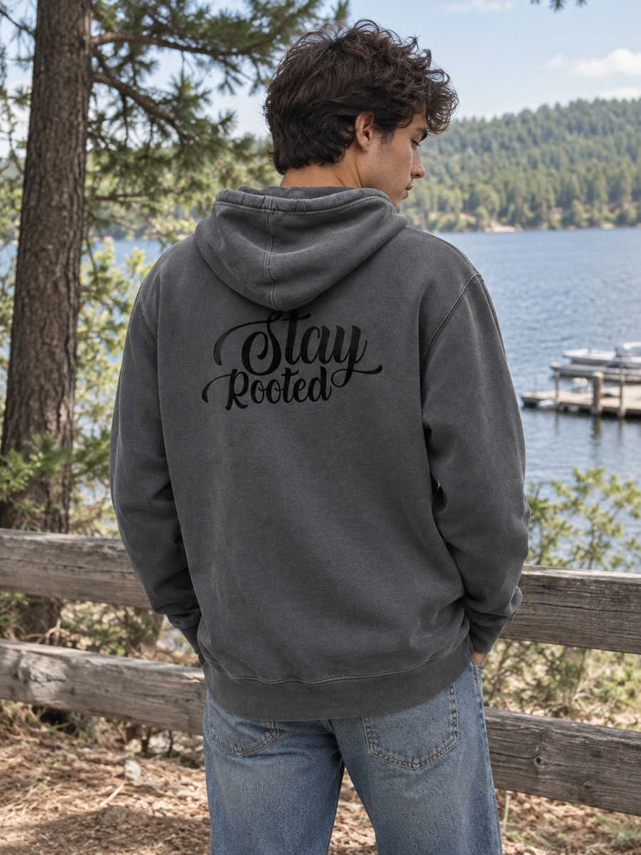 Stay Rooted Unisex Pigment-Dyed Hoodie Sweatshirt — Man beside lakeside wooden fence, back print visible