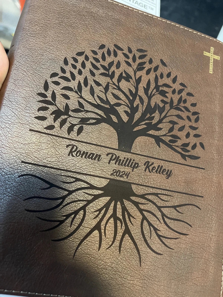 A hand holding a brown Bible with a full-cover tree design and Ronan Phillip Kelley 2024 engraved at the bottom