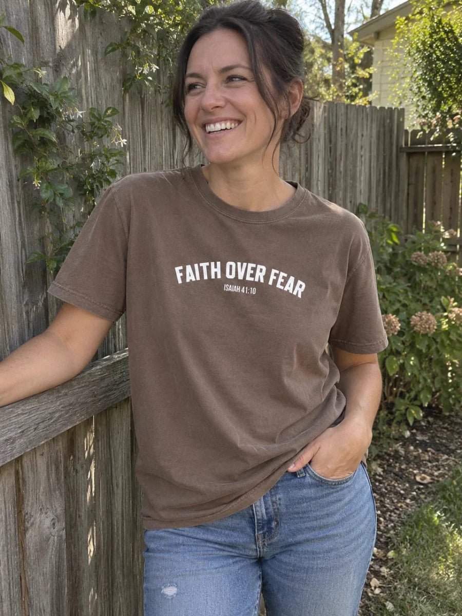 Brown Faith Over Fear tee styled with jeans beside a garden fence